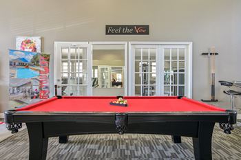A pool table with a red cloth and a sign that says "Feel the Vibe" above it.